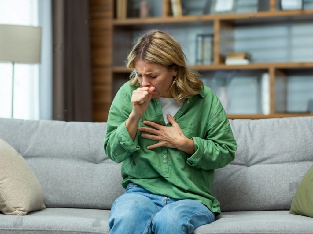 Woman sitting on couch sneezing and coughing