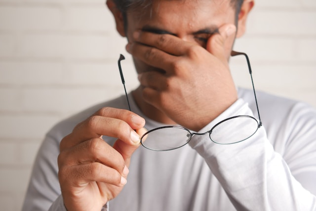Man with glasses rubbing his eyes
